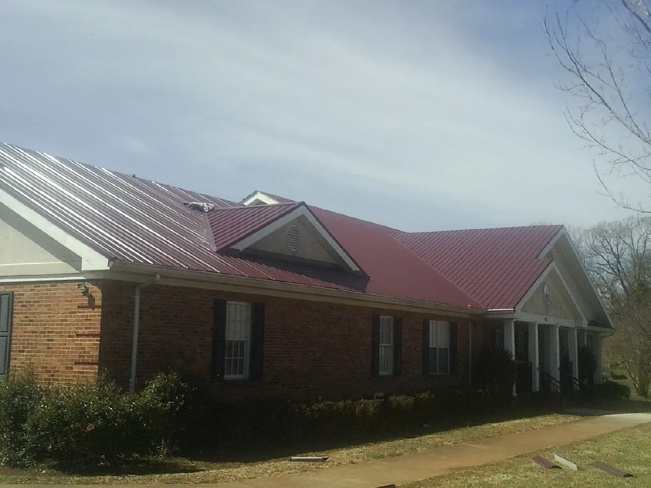 Red metal roof with gabled entries on a long brick building, from a Hail Damage Roof Repair job in Sheffield