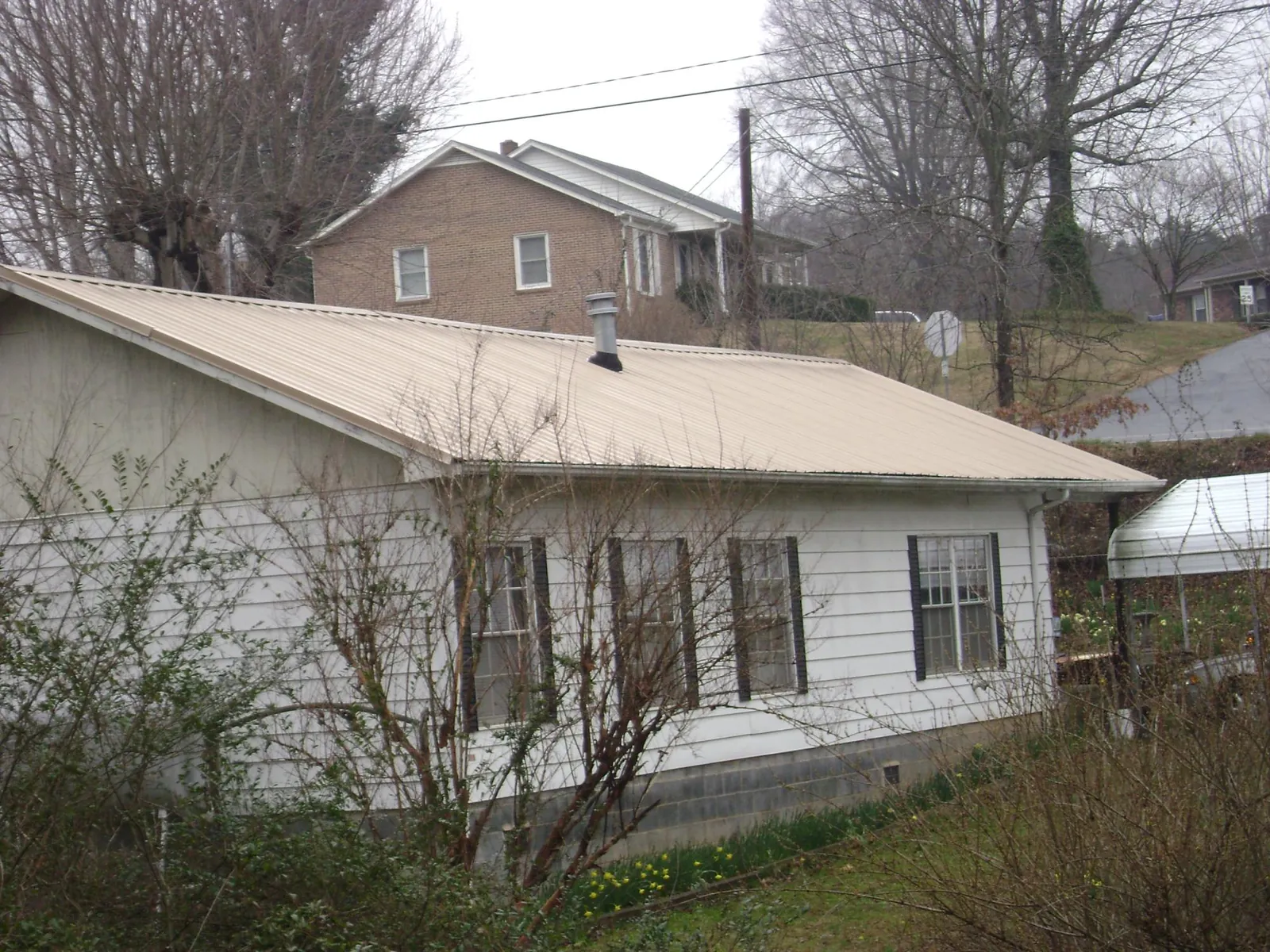 Tan metal roof on a white sided house set into a hillside — Commercial Roofing by Roofing Brothers in Sheffield
